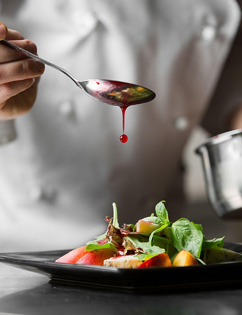 A chef plating up food and drizzling a sauce onto the food