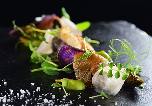 A leafy dish with flowers served upon a slate