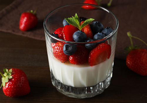 A fruit dessert with strawberries and blueberries in a glass with cream.